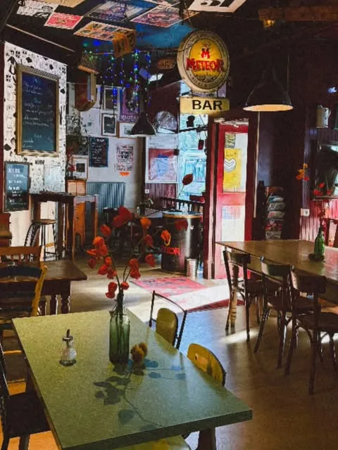La salle du Troc'afé : tables vertes, affiches au plafond et enseigne « Bar »